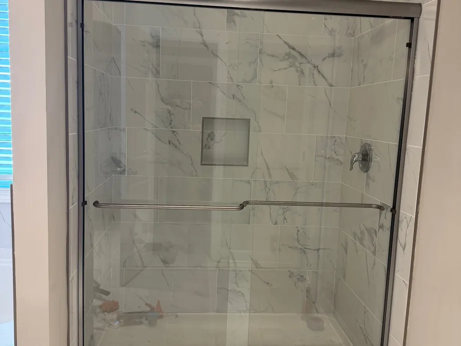Sliding glass shower door installed on a marble-look tiled shower